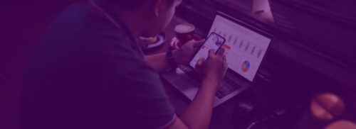 Profissional analisando métricas de tráfego pago em laptop e smartphone, com gráficos de performance e dados de campanhas digitais.